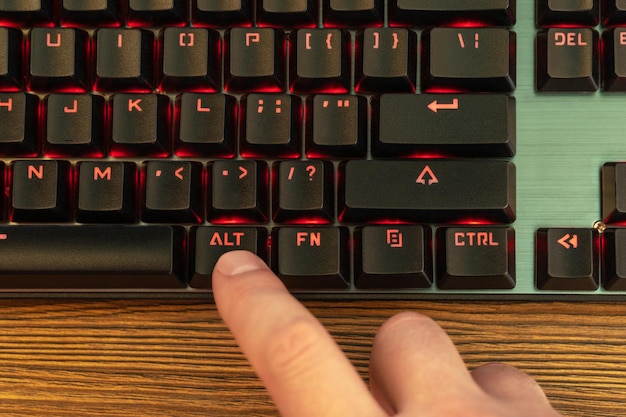 la main masculine appuie sur la touche alt du clavier noir avec rétroéclairage rouge