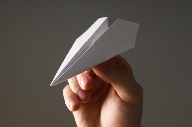 Main masculine avec avion en papier sur fond gris
