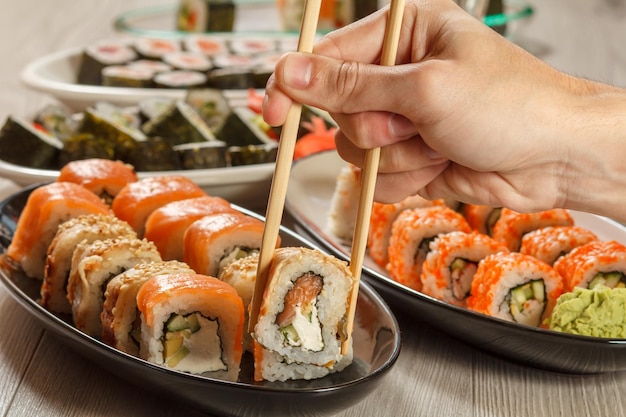 Main masculine avec des baguettes tenant un rouleau d'Uramaki avec Conger et différents rouleaux de sushi aux fruits de mer
