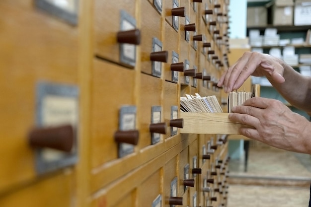 Une main masculine cherchant des cartes dans un vieux catalogue de cartes en bois