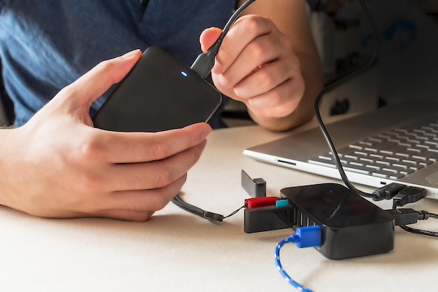 Main masculine connectant le disque dur avec un câble USB à un ordinateur portable et un répartiteur USB