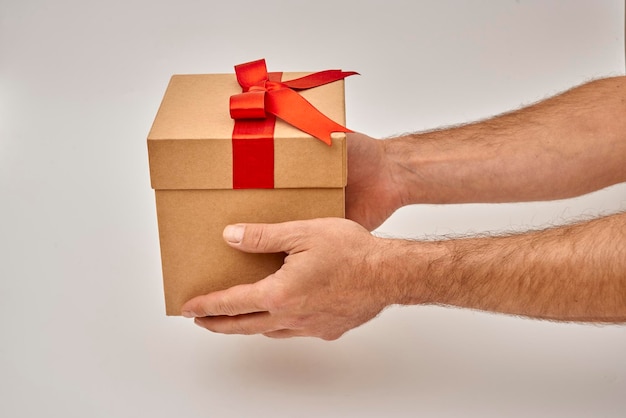 Main masculine donnant une boîte cadeau avec ruban rouge sur fond blanc
