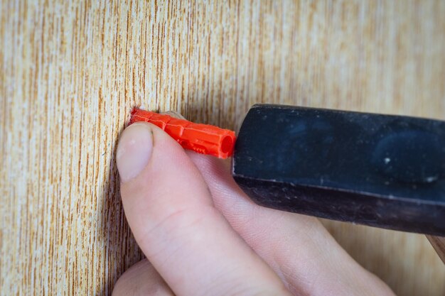 La main masculine enfonce la cheville dans le mur avec un marteau La cheville est martelée dans le gros plan du mur