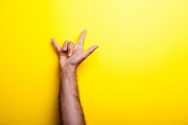 Main masculine faisant des signes avec ses doigts sur fond jaune