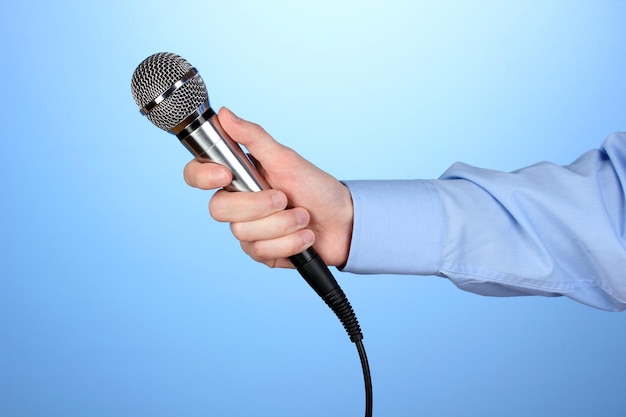 Main masculine avec microphone sur fond bleu