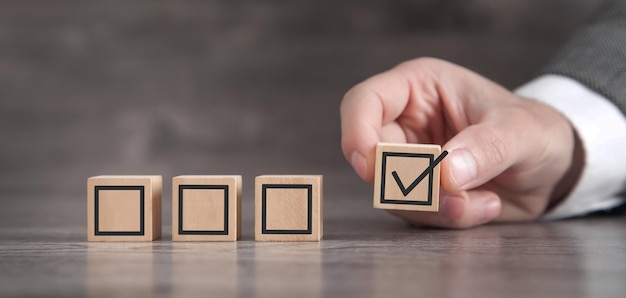 Main masculine montrant la case à cocher sur des cubes en bois Concept d'entreprise de votre choix