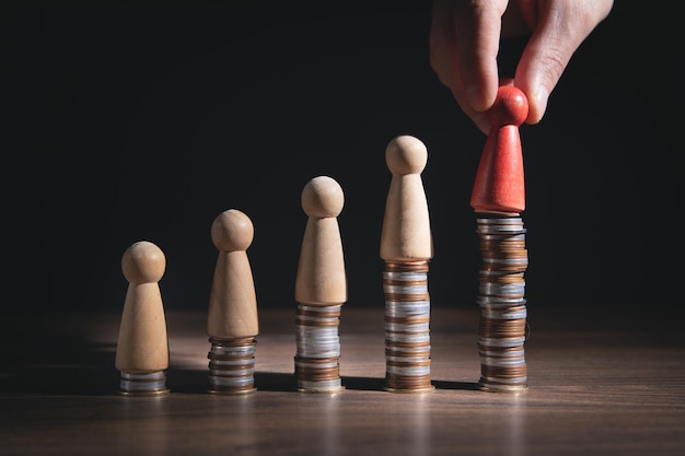 Main masculine montrant une figure humaine en bois sur une pile de pièces.