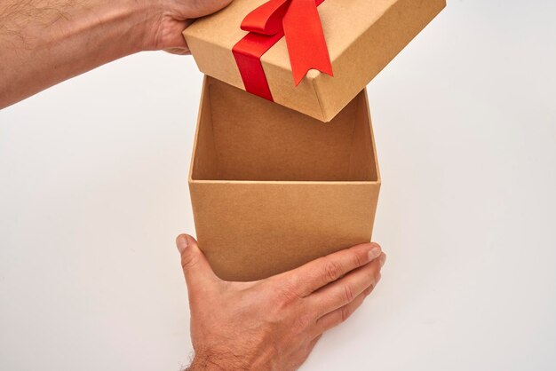 Main masculine ouvrant une boîte cadeau brune avec un ruban rouge sur fond blanc