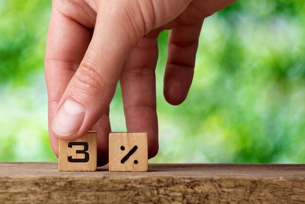 La main masculine présente des cubes en bois avec trois pour cent sur un fond vert