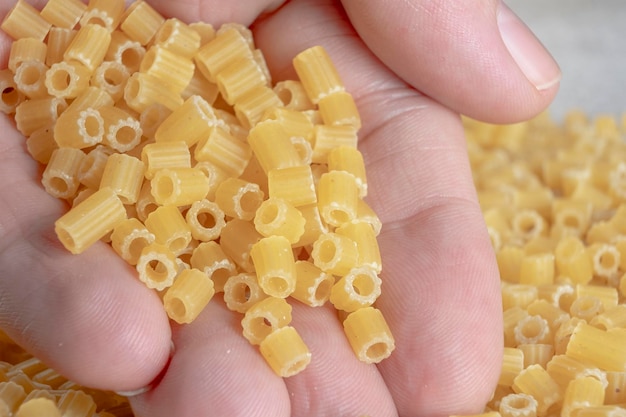 Une main masculine tenant un tas de pâtes courtes à tubes côtelés. Gastronomie méditerranéenne.