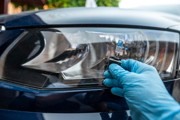 La main masculine tient une ampoule halogène contre les phares, le tout pour réparer la voiture