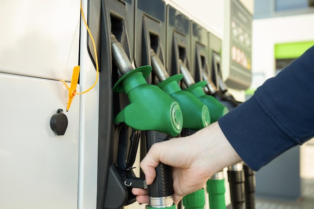 La main masculine tient le concept de pistolet de ravitaillement en carburant d'une voiture