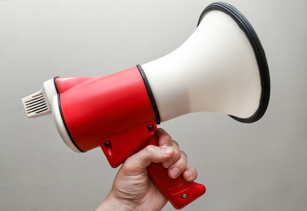 La main masculine tient un mégaphone à la main sur un fond blanc.