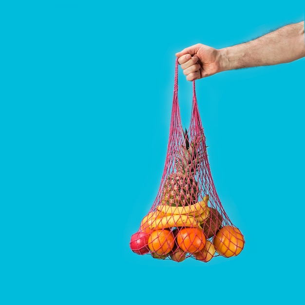 La main masculine tient un sac à provisions avec des sacs à provisions - ananas, oranges. Écologie conceptuelle bienveillante