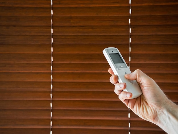 la main masculine tient une télécommande pour ouvrir les stores en bois