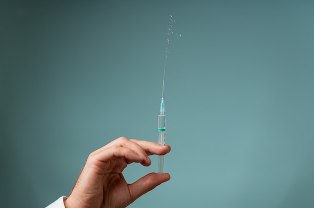 Main d'un médecin tenant une aiguille de seringue avec le médicament en éclaboussant. Sur fond bleu avec espace de copie.