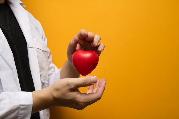 Main de médecin tenant un coeur rouge sur fond jaune Don de médecine cardiologie et concept de soins de santé