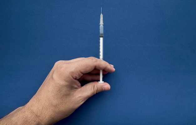 Main de médecin tenant une seringue pour vacciner avec un fond bleu et un espace de copie
