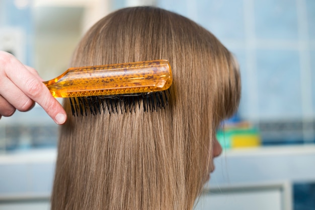 Main de mère avec brosse peigner les cheveux long blonde de fille enfant mignon après le bain sur fond intérieur flou.