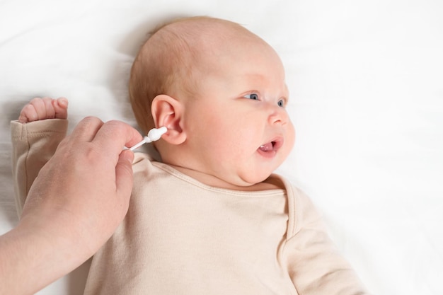 La main de la mère nettoie les oreilles de la petite fille avec un coton-tige