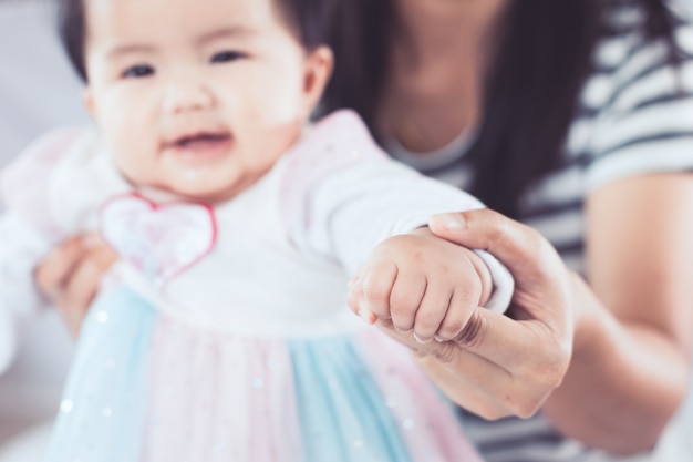 Main de mère tenant la main de bébé asiatique pour aider sa fille à se lever et marcher avec amour