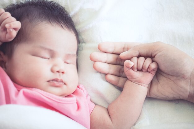 Main de mère tenant la main de bébé nouveau-né asiatique pendant qu&#39;elle dort avec amour