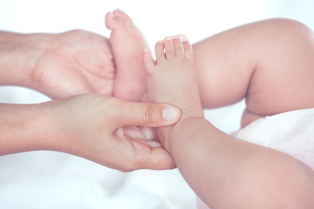 Main de mère tenant les petits pieds de la petite fille alors qu&#39;elle se trouve sur le lit