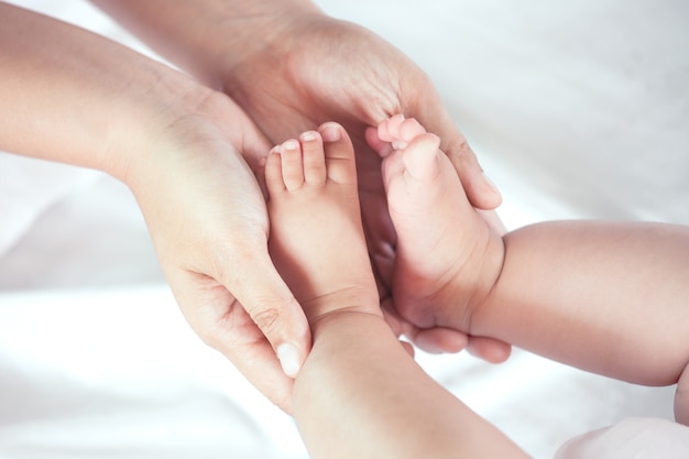 Main de mère tenant les petits pieds de la petite fille alors qu&#39;elle se trouve sur le lit