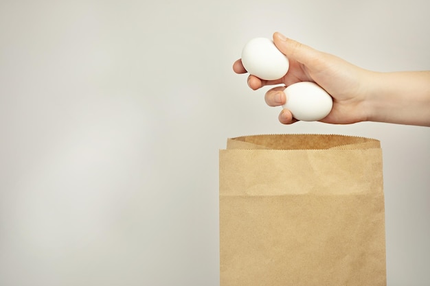 Une main met des oeufs blancs dans un paquet sur un fond blanc