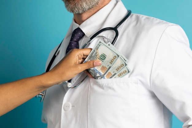 Main mettant des billets en dollars dans la poche du manteau du médecin recadrée