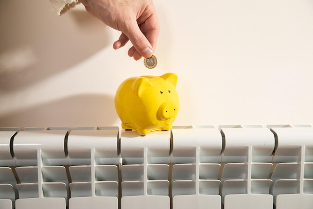 Main mettant la pièce dans la tirelire sur le radiateur de chauffage