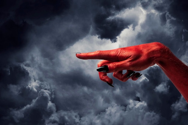 Main de monstre diable rouge Halloween avec des ongles noirs contre un ciel sombre