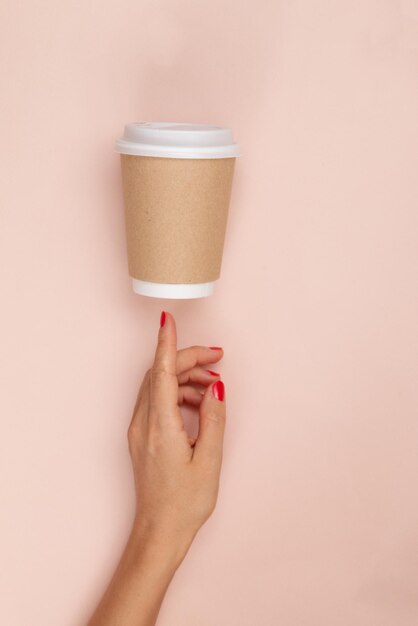 main montrant une tasse en papier fond rose