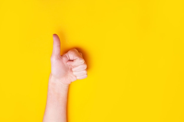 Photo la main montre les pouces vers le haut sur un fond jaune. concept d'approbation de classe