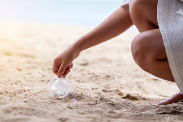 Une main nettoyant et ramassant une poubelle en verre en plastique sur la plage