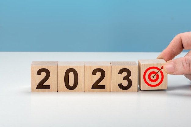 Main d'objectif 2023 mettant des cubes en bois 2023 avec l'icône d'objectif sur la table et l'espace de copie de fond bleu Commencer la nouvelle année 2023 avec le plan d'objectifs