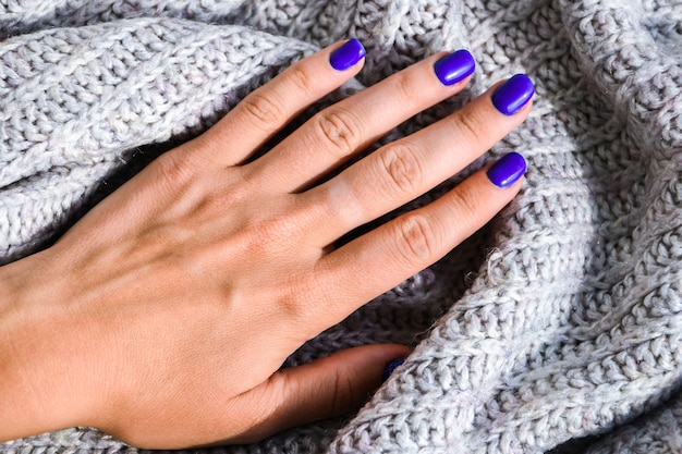 Photo main avec des ongles bleus sur fond de pull. manucure féminine. glamour belle manucure. soin de soi et de la peau.