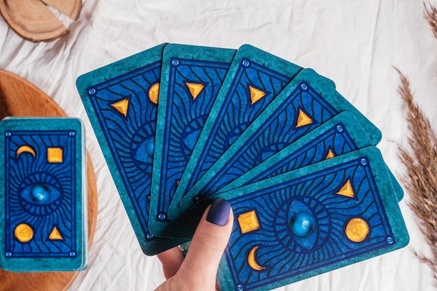 Une main avec des ongles bleus tient des cartes de tarot déployées sur une feuille de tissu blanc avec des épillets. Minsk, Biélorussie - 27.09.2021