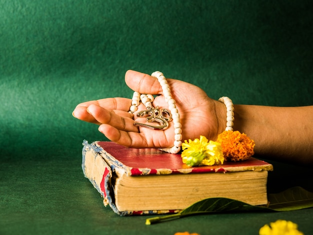 Main ouverte montrant le médaillon d'Aum avec des perles, un livre hindou rouge à la surface avec des fleurs