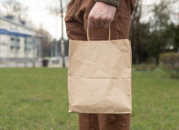 Main avec un pack d'artisanat brun ou un paquet à la main sur fond de ville et d'herbe.