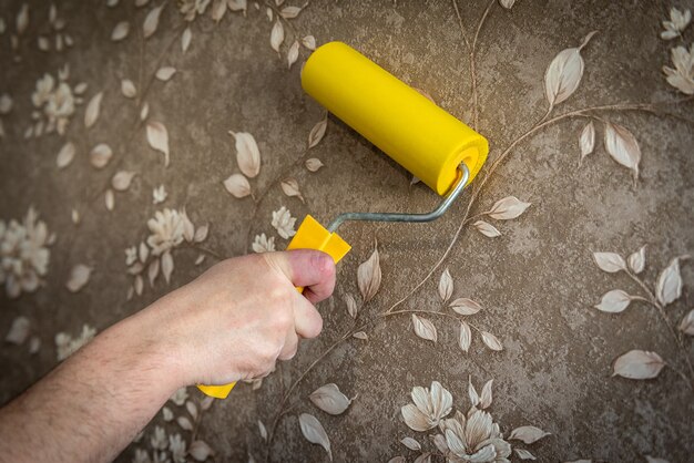 Main avec papier peint de lissage au rouleau sur le mur.