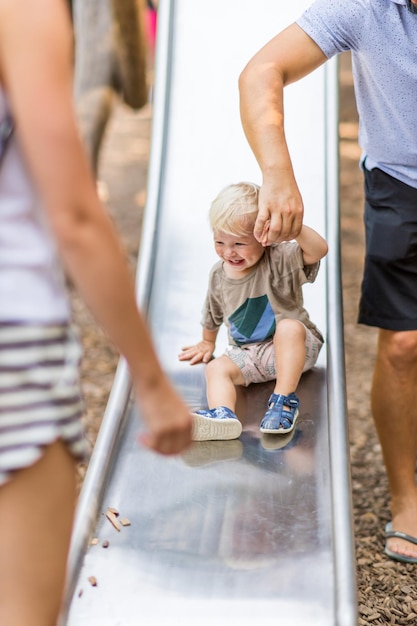 La main d'un parent tenant un petit bébé pendant qu'il glisse sur un terrain de jeu urbain par un été ensoleillé