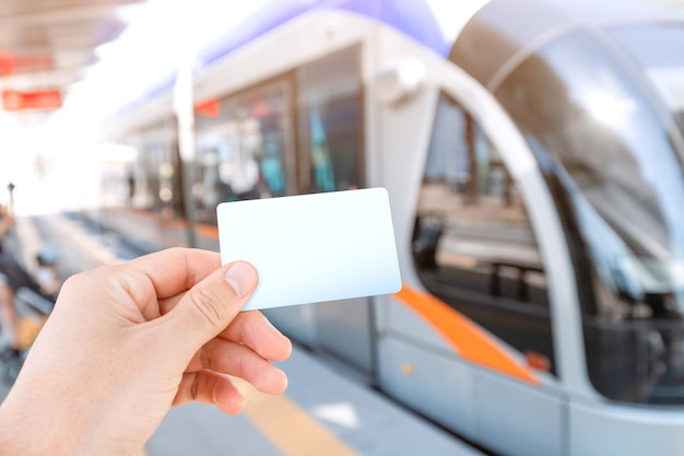 Main d'un passager tenant une carte vide blanche pour payer sans contact et sans numéraire pour le système de transport urbain moderne dans la ville