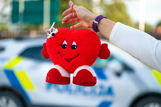Main avec une peluche en forme de coeur sur un fond défocalisé d'une voiture de police