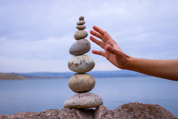 La main d'une personne atteint une pile de rochers avec le ciel en arrière-plan.