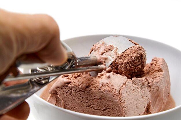 La main d'une personne avec une cuillère à crème glacée ramasse de la glace au chocolat dans un bol blanc