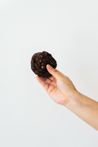 Photo main d'une personne méconnaissable tenant un cookie aux pépites de chocolat sur fond blanc