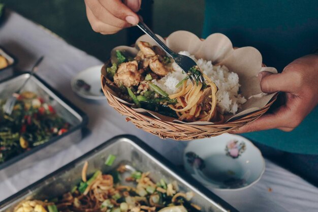 La main de la personne met des nouilles frites blanches de la poêle en acier à une assiette en bois pendant le déjeuner au restaurant