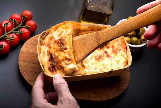 Photo main de personne prenant une tranche de lasagne avec une spatule en bois