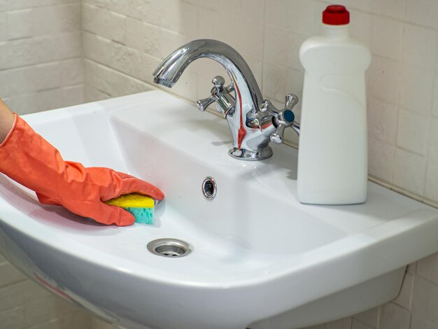 Main de personne tenant une éponge à la menthe pour nettoyer le lavabo et le robinet de la salle de bain